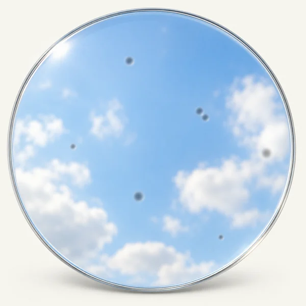 A round lens view of blue sky with a few small, soft grey dots scattered across it.